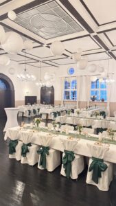Eleganter Hochzeitssaal, weiße Tischdecken, grüne Schleifen, Papierlampions.