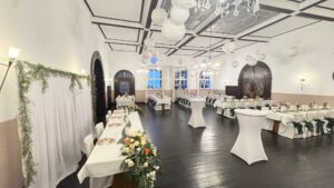 Großer Festsaal mit weißen Tischdecken, Blumenarrangements und runden Lampen.